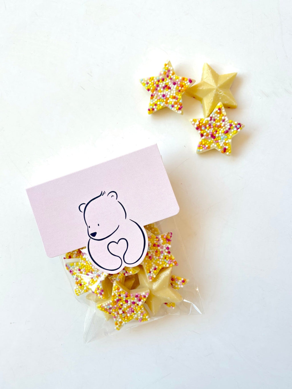 Star-shaped sugar cookies with colorful sprinkles, shown with a small clear bag and a pink card featuring a teddy bear illustration, on a white background.
